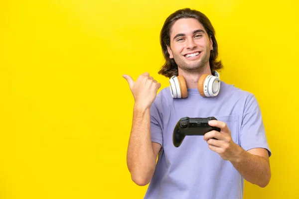 stock image Young handsome caucasian man playing with a video game controller over isolated on yellow background pointing to the side to present a product