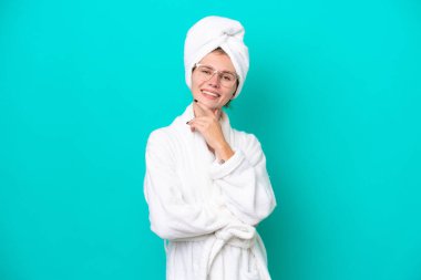 Bornozlu genç bir kadın mavi arka planda gözlüklü ve gülümseyen.