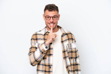 Beyaz arka planda izole edilmiş beyaz tenli yakışıklı bir adam sessiz bir jest işareti gösteriyor. Parmağını ağzına sokuyor.