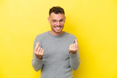 Sarı arka planda izole genç beyaz yakışıklı adam para hareketi yapıyor.
