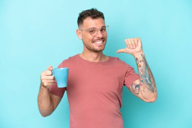 Kafkasyalı genç bir adam elinde bir fincan kahve tutarken mavi arka planda izole edilmiş gururlu ve kendinden memnun.