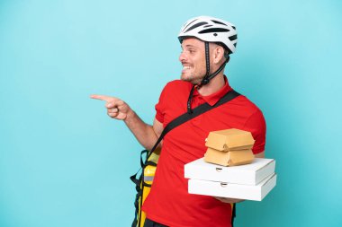 Termal sırt çantalı beyaz bir genç ve elinde mavi arka planda izole edilmiş fast food tutuyor.