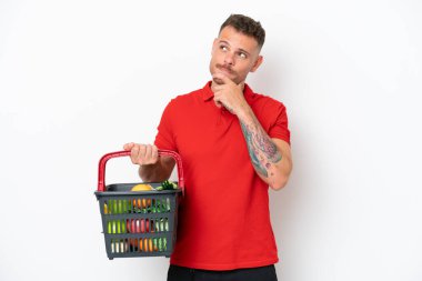 Beyaz arka planda izole edilmiş yiyecek dolu bir alışveriş sepeti tutan beyaz bir adam.