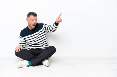 Genç adam beyaz arka planda izole bir şekilde yerde oturuyor.