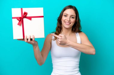 Young caucasian woman holding a gift isolated on blue background and pointing it