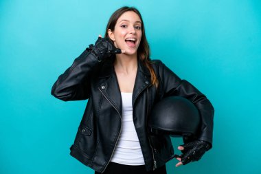 Motosiklet kasklı, mavi arka planda izole edilmiş, telefon jesti yapan beyaz bir kadın. Bana geri dönüş işareti ver.