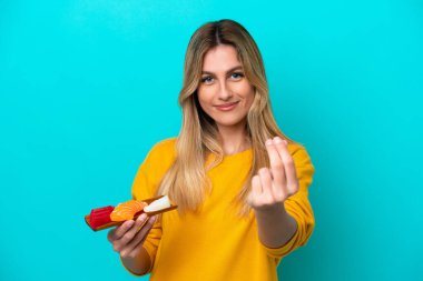 Uruguaylı genç bir kadın mavi arka planda saşimi tutuyor ve para hareketi yapıyor.