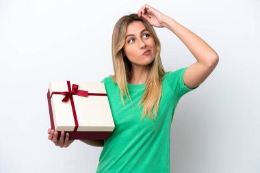 Genç Uruguaylı kadın elinde beyaz arka planda izole edilmiş bir hediye tutuyor. Şüpheleri var ve kafası karışmış bir yüz ifadesi var.