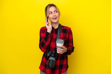 Uruguaylı fotoğrafçı kadın sarı arka planda izole edilmiş. Elinde kahve ve cep telefonu var.