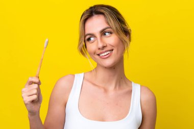 Genç Uruguaylı dişlerini fırçalayan kadın mutlu bir ifadeyle sarı arka planda izole edilmiş.