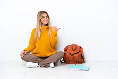 Uruguayan student woman sitting one the floor isolated on white background pointing to the side to present a product