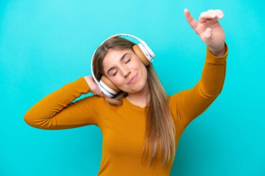 Genç beyaz kadın mavi arka planda izole edilmiş müzik ve dans dinliyor.