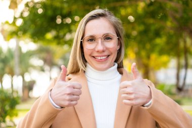 Açık havada genç sarışın bir kadın Gözlüklü ve başparmağıyla