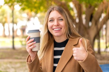 Genç, güzel, sarışın bir kadın açık havada kahvesini yudumluyor. Çünkü iyi bir şey oldu.