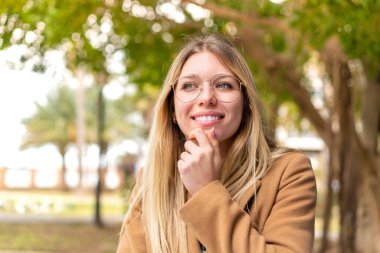 Açık havada güzel sarışın bir kadın yan tarafa bakıyor.