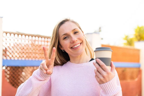 Mladá Blondýnka Žena Drží Odnést Kávu Venku Usmívá Ukazuje Vítězství — Stock fotografie