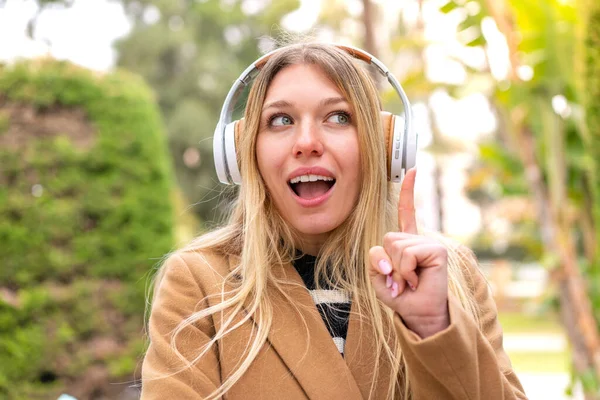Mladá Hezká Blondýnka Poslouchající Hudbu Sluchátky Venku Přemýšlející Nápadu Ukazovat — Stock fotografie