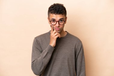 Genç Brezilyalı adam bej arka planda izole edilmiş ve düşünüyor