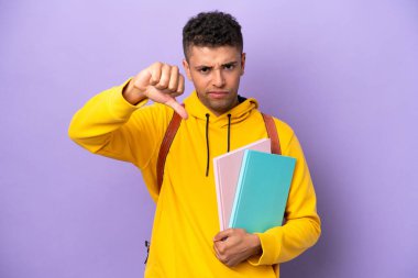 Young student Brazilian man isolated on purple background showing thumb down with negative expression