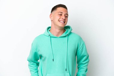 Beyaz arka planda izole edilmiş genç Brezilyalı adam kolları kalçasında ve gülümsüyor.