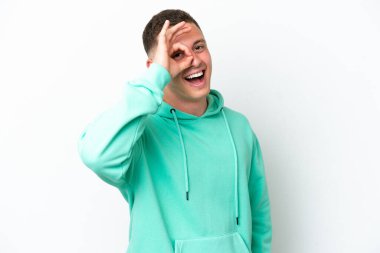 Beyaz arka planda izole edilmiş genç Brezilyalı adam parmaklarıyla tamam işareti gösteriyor