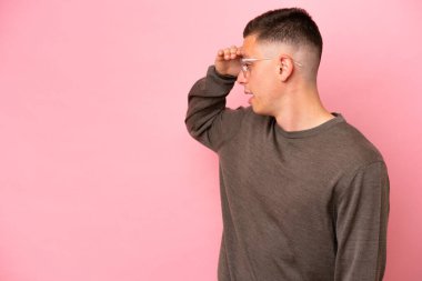 Pembe arka planda mahsur kalmış Brezilyalı genç bir adam sürpriz bir ifadeyle yan tarafa bakıyor.