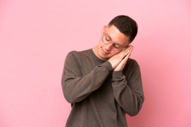 Pembe arka planda izole edilmiş genç Brezilyalı adam uyku jesti yapıyor.