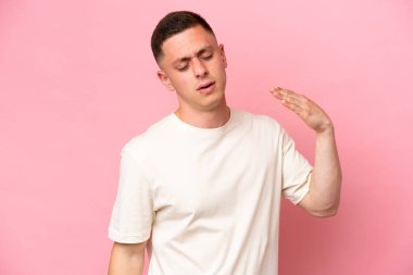 Genç Brezilyalı adam pembe arka planda izole edilmiş, yorgun ve hasta bir ifadeyle.