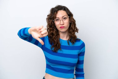 Beyaz arka planda izole edilmiş genç beyaz kadın olumsuz ifade ile baş parmağını aşağı gösteriyor.