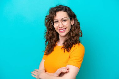 Genç beyaz kadın mavi arka planda izole edilmiş, mutlu bir ifadeyle gözlüklü.