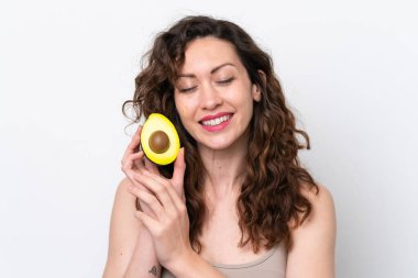 Beyaz arka planda izole edilmiş beyaz bir kadın elinde bir avokado tutarken gülümsüyor. Portreyi kapat