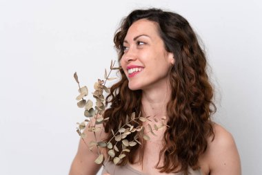 Beyaz arka planda, elinde okaliptüs dalıyla gülümseyen beyaz bir kadın. Portreyi kapat