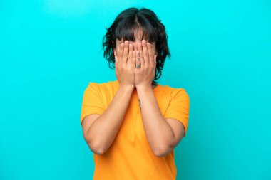 Arjantinli genç bir kadın mavi arka planda tek başına gözlerini elleriyle kapatıyor.