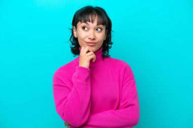 Genç Arjantinli kadın mavi arka planda izole edilmiş bir şekilde bakarken bir fikir düşünüyor.