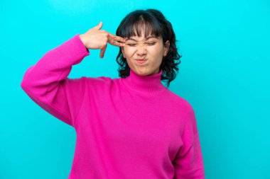 Genç Arjantinli kadın mavi arka planda izole edilmiş ve intihar jesti yapmada sorun yaşıyor.