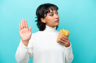 Arjantinli genç bir kadın elinde kızarmış cipslerle mavi arka planda izole bir şekilde duruyor.