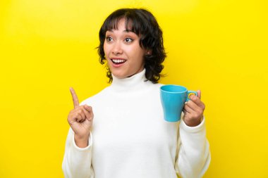 Arjantinli genç bir kadın sarı arka planda izole edilmiş bir fincan kahve tutuyor. Çözümün farkına varmak için parmağını kaldırıyor.