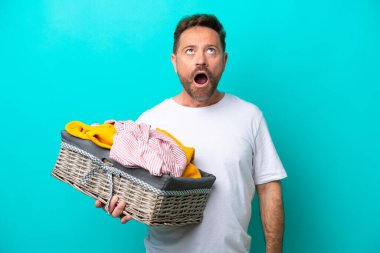 Mavi arka planda bir çamaşır sepetini tutan orta yaşlı kadın şaşırmış bir ifadeyle yukarı bakıyor.