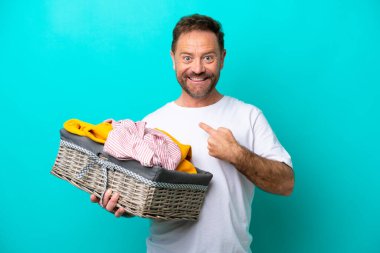 Mavi arka planda yüzü sürpriz bir ifadeyle izole edilmiş çamaşır sepeti tutan orta yaşlı bir kadın.