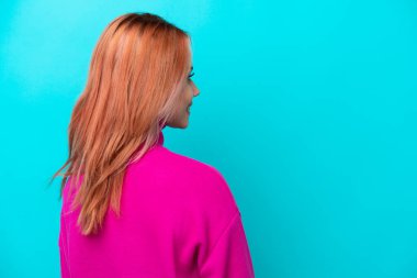 Genç Rus kadın mavi arka planda izole edilmiş. Arka tarafta ve yan tarafa bakıyor.