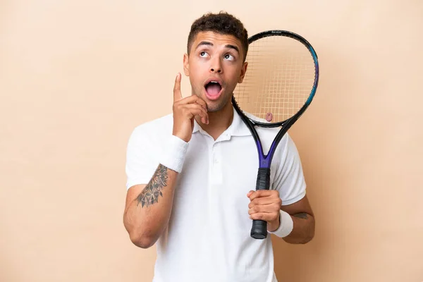 stock image Young brazilian handsome man playing tennis isolated on beige background thinking an idea pointing the finger up