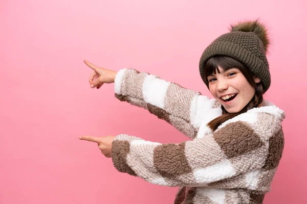 小高加索女孩 冬季夹克 粉色背景隔离 手指指向侧面 并展示了一种产品 — 图库照片