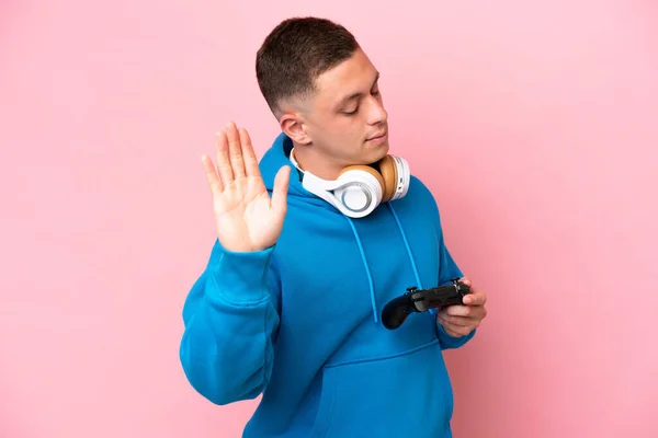 年轻的巴西男子玩一个视频游戏控制器孤立的粉色背景使停止手势和失望 — 图库照片