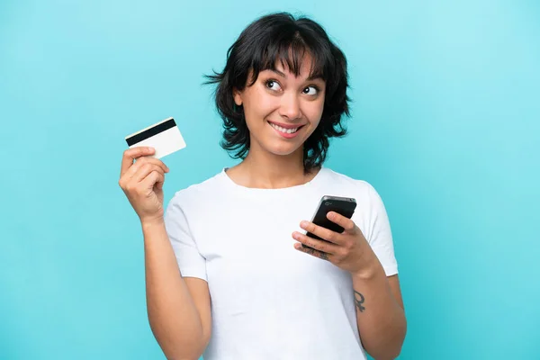 Fiatal Argentin Elszigetelt Kék Háttér Vásárol Mobil Hitelkártyával Miközben Gondolkodás — Stock Fotó