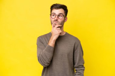 Kafkasyalı genç adam sarı arka planda izole edilmiş bir şekilde yukarı bakarken bir fikir düşünüyor.