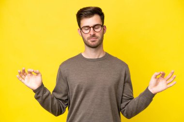 Zen pozisyonunda sarı arka planda izole edilmiş genç beyaz adam.