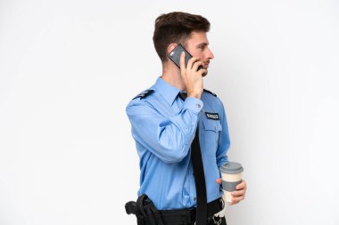 Beyaz arka planda izole edilmiş genç bir beyaz adam elinde kahve ve bir cep telefonu tutuyor.