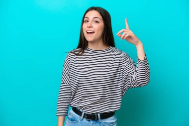 Kafkasyalı genç kadın mavi arka planda izole edildi. Çözümün farkına varmak için parmağını kaldırdı.