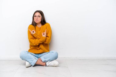 Beyaz arka planda izole bir şekilde yerde oturan genç kız, yan taraftakilerin şüpheye düştüğünü gösteriyor.