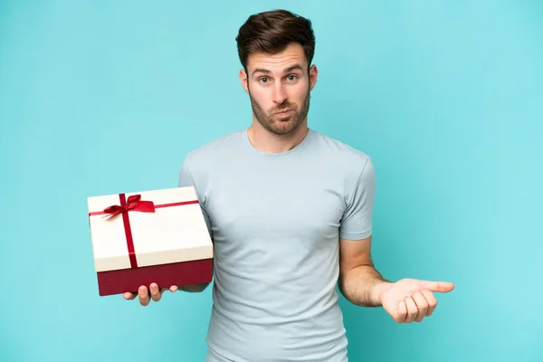 Young Caucasian Man Holding Gift Isolated Blue Background Making Doubts — Stock Photo, Image